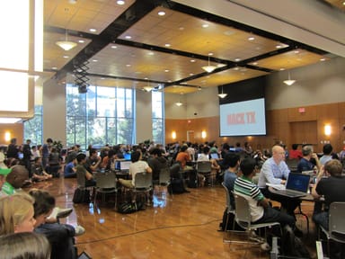 Hundreds of developers working on laptops at a HackTX hackathon in a large hall